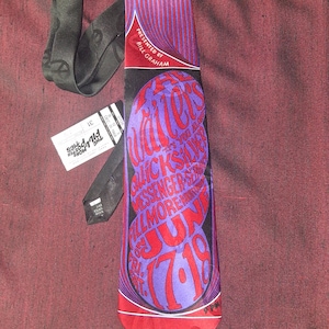 May include: A red and purple silk tie with a graphic design featuring the text "The Waters" and "June 17, 1969". The tie is presented by Bill Graham.