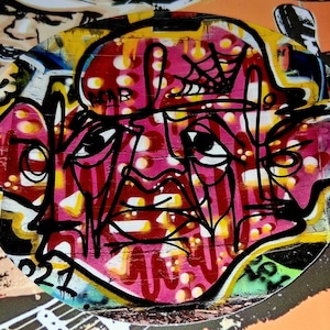 May include: Abstract graffiti art featuring a stylized face in shades of pink, red, and black. The artwork is set against a background of yellow, white, and orange, with additional graffiti elements. The design includes a spiderweb and the number "021".