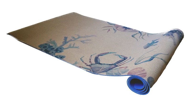 May include: A rolled-up yoga mat with a blue border and a light brown surface. The mat features a watercolour design of blue and pink sea life, including a crab, coral, and seaweed.