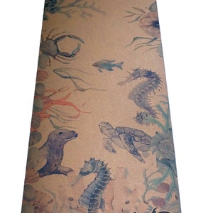 May include: A cork yoga mat featuring a watercolour design of sea creatures, including a crab, seahorse, turtle, and fish. The mat is brown with a light brown background and has the text "US Upward Salute" in black at the bottom.