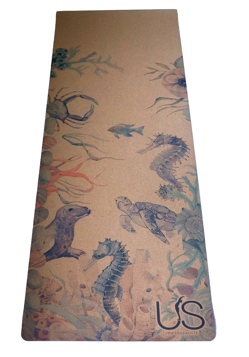 May include: A cork yoga mat featuring a watercolour design of sea creatures, including a crab, seahorse, turtle, and fish. The mat is brown with a light brown background and has the text "US Upward Salute" in black at the bottom.
