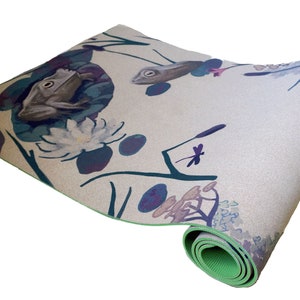 May include: A rolled-up yoga mat with a green border and a nature-inspired design featuring frogs, dragonflies, and flowers on a light beige background.
