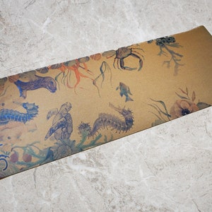 May include: A brown yoga mat with a sea life design. The mat features seahorses, a crab, a turtle, and seaweed. The text "US" is printed on the bottom left corner of the mat.