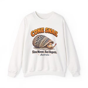 May include: A white long-sleeve sweatshirt featuring a graphic of a cone snail with a patterned shell. The text reads CONE SNAIL, Slow Mover. Fast Regrets., and Australia. The snail has a tan body with brown spots and a determined facial expression.