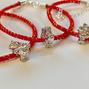 May include: Three red string bracelets with silver charms. Each charm is a different animal, including a dragon, a lion, and a pig.