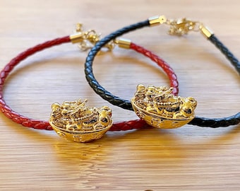 May include: Two leather bracelets with gold charms. The charms are detailed with a group of figures in a boat. One bracelet is red and the other is black.