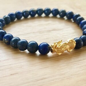 May include: A blue lapis lazuli beaded bracelet with a gold dragon charm.