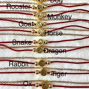 May include: A selection of gold charm bracelets, each displaying a Chinese zodiac symbol. The bracelets have a red cord and a gold chain. The zodiac animal names are printed on the image.
