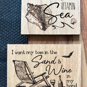 May include: Two wooden signs with a beach theme. The top sign has a seashell and the text "in serious need of some VITAMIN Sea". The bottom sign has a beach chair, a glass of wine, a bottle of wine, and the text "I want my toes in the Sand & Wine in my hand".