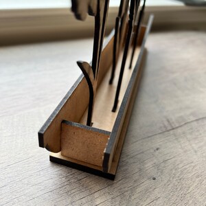 May include: A wooden flower stand with a black painted finish. The stand has a rectangular base with slots for holding flowers. The stand is made of plywood and has a rustic look.