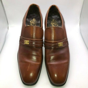 May include: A pair of brown leather slip-on shoes with a gold buckle detail. The shoes have a pointed toe and a low heel.