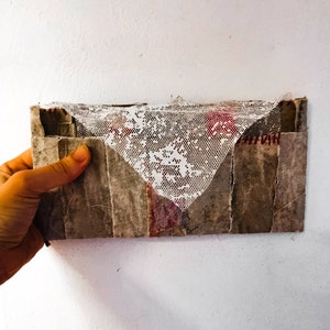 Carta a... sobre hecho de tela y cemento con un billete insertado en el interior.