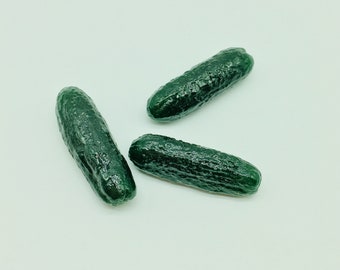 May include: Three dark green cucumbers with textured skin are arranged on a white background. The cucumbers are oblong in shape and vary slightly in size. The image is well-lit, highlighting the cucumbers' color and texture.