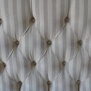 May include: Close-up of a tufted headboard with a striped fabric in shades of grey and white. The fabric is buttoned with round, silver buttons.