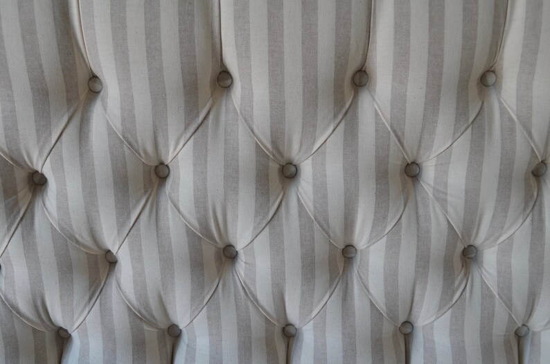 May include: Close-up of a tufted headboard with a striped fabric in shades of grey and white. The fabric is buttoned with round, silver buttons.