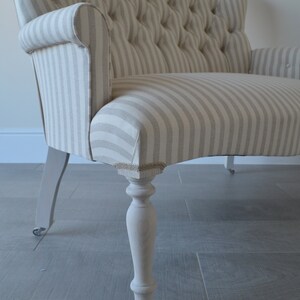 May include: A striped fabric loveseat with a tufted back and white painted legs. The loveseat has a curved front and is on wheels.