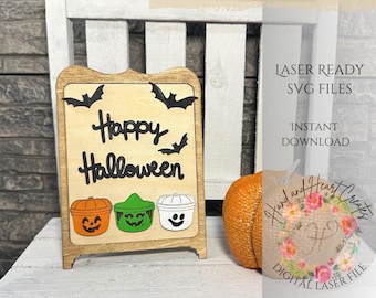 May include: A wooden sign with the text "Happy Halloween" and three Halloween-themed buckets. The sign is on a wooden easel and there is a small orange pumpkin in the background.