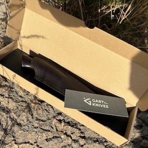 May include: A brown leather knife sheath with a dark wood handle. The sheath is in a cardboard box with a black card that says "GART KNIVES".