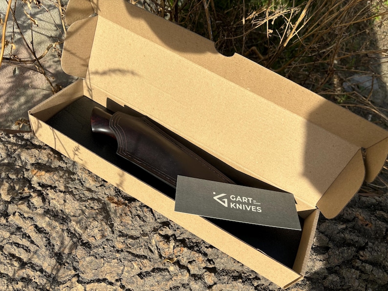 May include: A brown leather knife sheath with a dark wood handle. The sheath is in a cardboard box with a black card that says "GART KNIVES".