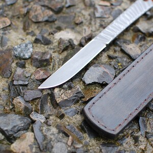 May include: A silver knife with a leather sheath. The knife has a textured blade and the sheath has a stitched edge.