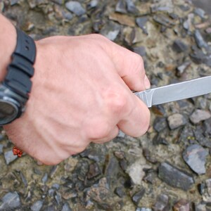 May include: A person's hand holding a silver knife with a black handle. The knife is sharp and has a pointed tip. The hand is wearing a black watch with a digital display.