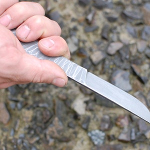 May include: A silver knife with a textured handle is held in a hand. The knife has a sharp point and a straight blade.