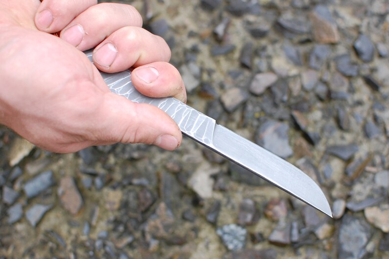 May include: A silver knife with a textured handle is held in a hand. The knife has a sharp point and a straight blade.