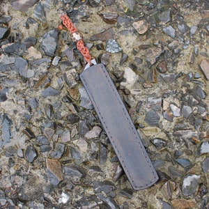 May include: A brown leather knife sheath with a red and white braided cord.