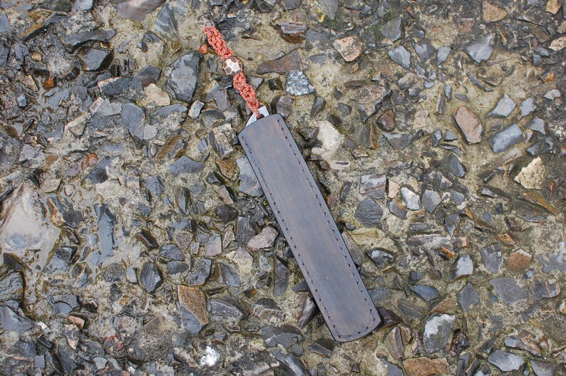May include: A brown leather knife sheath with a red and white braided cord.