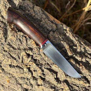 May include: A hunting knife with a dark wood handle and a silver metal bolster. The blade is made of stainless steel and has a satin finish.