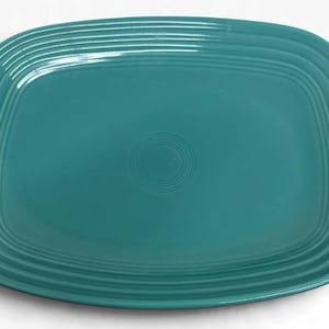 May include: A rectangular teal ceramic serving platter with rounded corners, featuring a series of concentric embossed rings along the raised rim and a small circular ring pattern centered in the middle of the flat surface.