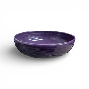 Pode incluir: Uma tigela de cerâmica roxa brilhante. Possui um formato largo e raso, com interior liso e exterior texturizado e canelado. A cor é um roxo profundo e vibrante, adequado para servir alimentos ou como elemento decorativo.