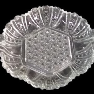 Könnte beinhalten: Eine klare Glasservierplatte mit sechseckiger Mitte und verzierten, gewellten Rändern. Die Platte hat ein zartes, filigranes Design.