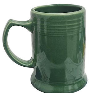 May include: A green ceramic mug with a handle. The mug has a cylindrical shape with a slightly flared base and a ridged design around the top. The mug is approximately 13 cm tall.