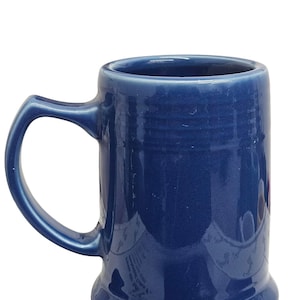 May include: A cobalt blue ceramic mug with a rounded base and a large, curved handle. The mug has a glossy finish and a simple, classic design, suitable for coffee or tea.
