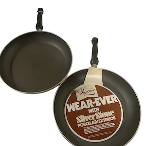 Könnte beinhalten: Zwei braune Antihaft-Bratpfannen mit schwarzen Griffen. Die größere Pfanne hat ein Etikett mit der Aufschrift "Superior Wear-Ever with SilverStone Porcelain Exterior".