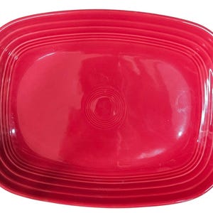 May include: A vibrant red rectangular serving platter. The platter has rounded corners and a slightly raised rim with concentric ridges. The center of the platter features a circular design. This piece is suitable for serving food.