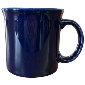 May include: A dark blue ceramic mug with a rounded body and a curved handle. The mug has a glossy finish and a simple, classic design. The mug is empty and ready to be filled with a beverage.