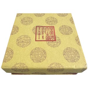 Puede incluir: Caja cuadrada cerrada con fondo amarillo claro y patrones circulares repetidos. La caja tiene un sello rectangular rojo con caracteres chinos. La caja está hecha de papel y tiene una superficie texturizada.