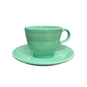 Può includere: Un set tazza e piattino verde menta. La tazza ha una forma arrotondata con manico e dettagli a coste orizzontali. Il piattino è circolare e corrisponde al colore della tazza. Il set è in ceramica.