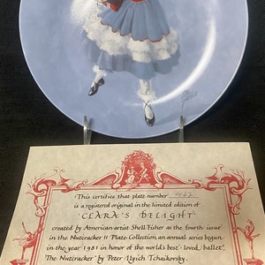 May include: A certificate of authenticity for a limited edition collectible plate featuring a young girl in a blue dress holding a toy. The plate is titled "Clara's Delight" and is part of the Nutcracker II Plate Collection. The certificate is signed by John B.  Hagan, President.