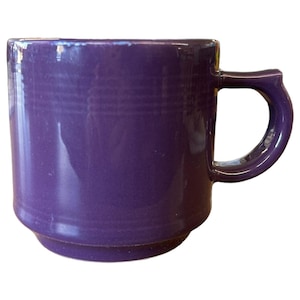 May include: A solid purple ceramic mug with a rounded base and a curved handle. The mug has a glossy finish and a simple, classic design. This mug is perfect for enjoying coffee, tea, or any favorite beverage.