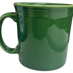 May include: A solid green ceramic mug with a curved handle. The mug has a slightly flared rim and a smooth, glossy finish. The mug is a vibrant shade of green.