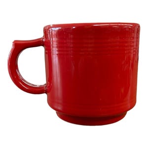 May include: A vibrant red ceramic mug with a rounded handle. The mug has a cylindrical shape with horizontal ridges near the top and bottom. The glossy finish reflects light, highlighting its smooth surface. A classic design for enjoying hot beverages.