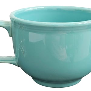Puede incluir: Una taza grande de cerámica turquesa con un cuenco redondeado y un asa robusta. La taza tiene un acabado brillante y un diseño sencillo y clásico, adecuado para servir sopa o bebidas. La taza es de color liso sin dibujos.