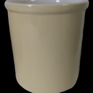 Może przedstawiać: Kremowy ceramiczny kubek z lekko rozszerzonym brzegiem i gładkim, matowym wykończeniem. Wnętrze jest białe, kontrastujące z zewnętrzną stroną. Kubek ma prosty, cylindryczny kształt.