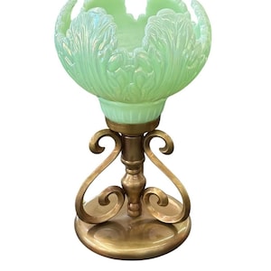 Peut inclure: Un bol en verre irisé vert clair avec un bord festonné en forme de feuille, soutenu par un support en métal doré comprenant un pilier central, deux volutes symétriques et une base circulaire.