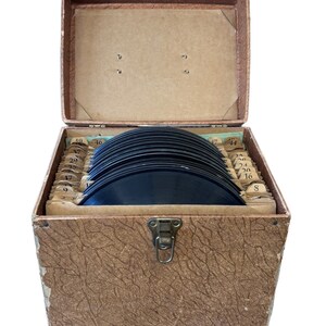 Könnte beinhalten: Eine braune, lederbezogene Box mit einem Scharnierdeckel, geöffnet, um einen Stapel schwarzer Schallplatten zu enthüllen. Die Schallplatten sind von 8 bis 46 nummeriert.