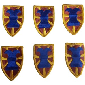 May include: Six embroidered patches in the shape of a shield with a gold border and a red centre. The centre of each patch features a blue stylised cannon with a yellow flame coming out of the top.