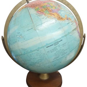 May include: A vintage Replogle globe with a light blue ocean and colorful continents. The globe is mounted on a wooden base with a brass meridian ring and a degree scale. The globe features detailed geographical information.